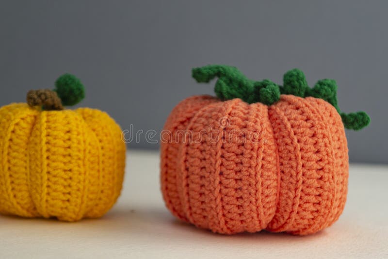 Uma boneca de crochê com roupa laranja e segurando abóboras