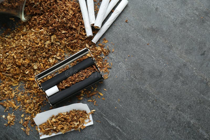 Flat lay composition with roller and tobacco on dark grey table. Making hand rolled cigarettes. Flat lay composition with roller and tobacco on dark grey table. Making hand rolled cigarettes