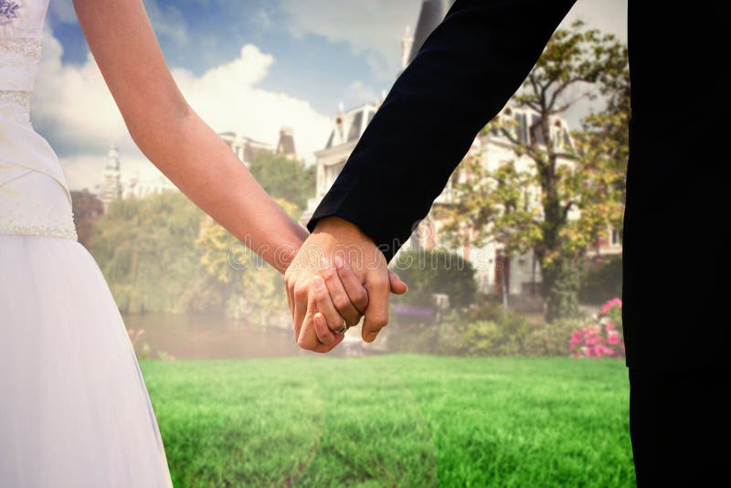 Mid section of newlywed couple holding hands in park against sunny day by the river. Mid section of newlywed couple holding hands in park against sunny day by the river