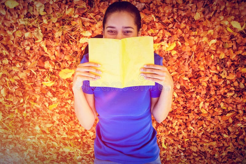 Pretty woman reading in the park against autumn leaves on the ground. Pretty woman reading in the park against autumn leaves on the ground