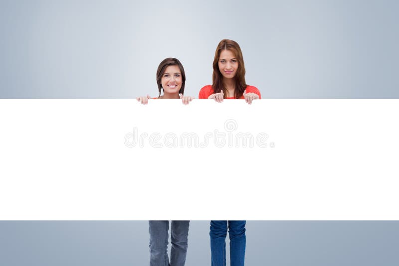 Composite image of smiling young women proudly holding a blank poster royalty free stock photography Composite image of smiling young women proudly holding a blank poster royalty free stock photography