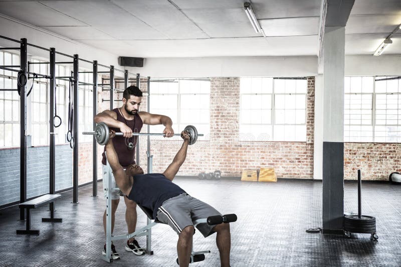 Composite image of trainer helping muscular man to lift the barbell stock images Composite image of trainer helping muscular man to lift the barbell stock images