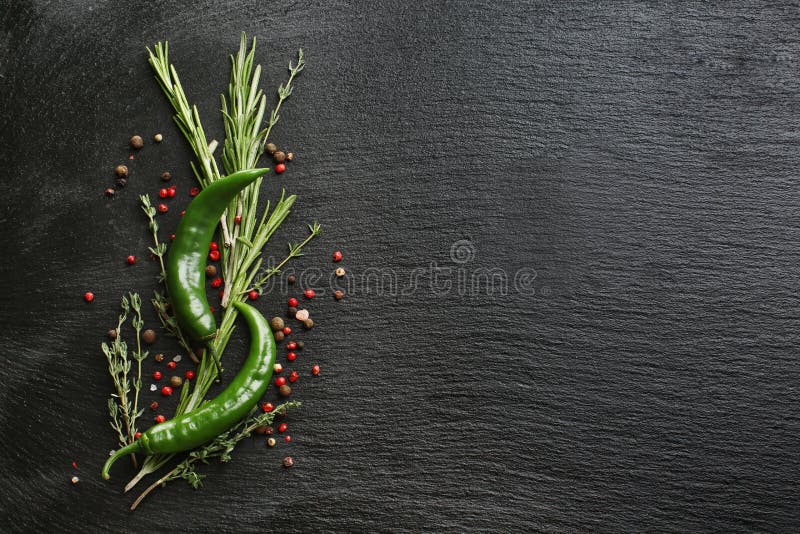 Composition avec le piment vert, les épices et les herbes fraîches sur le fond texturisé noir