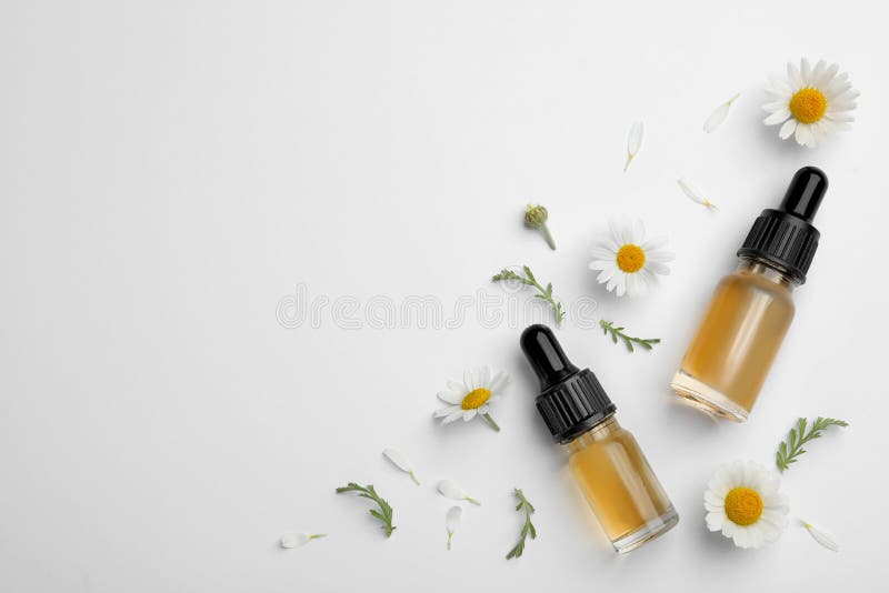 Composition with chamomile flowers and cosmetic bottles of essential oil on white background