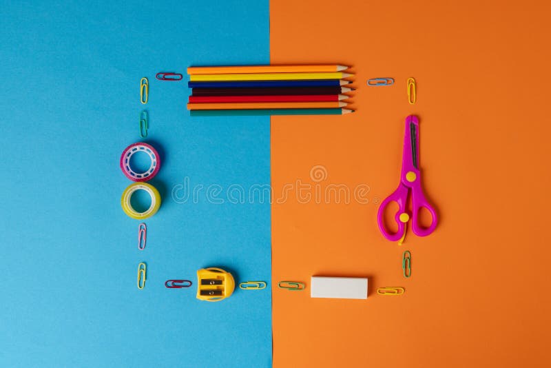 Composition of frame made of crayons, scissors and other items on blue and orange surface. School equipment, tools and creativity concept.