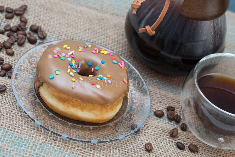 A composition of a glass coffee maker and a delicious maple donut