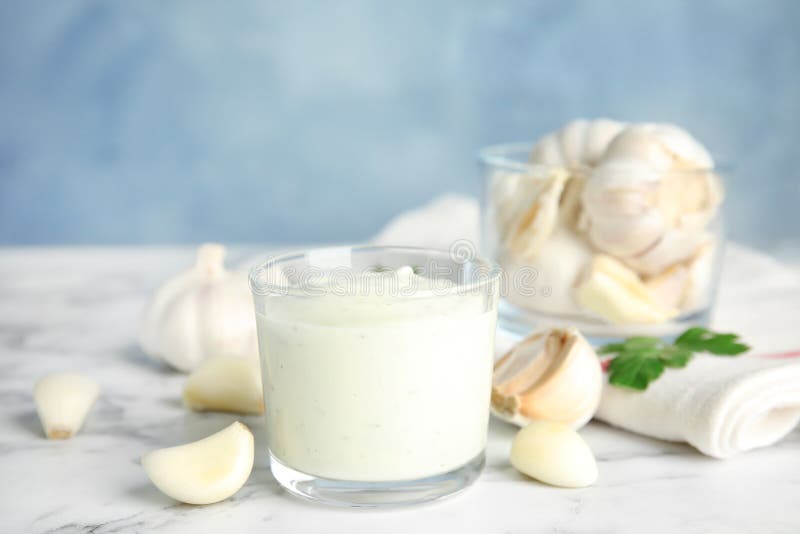 Composition with glass of garlic sauce on marble table.