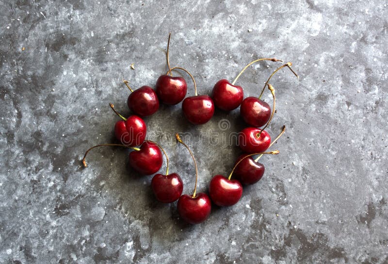 composition in heart shape with fresh cherries on dark background, top view. High quality photo