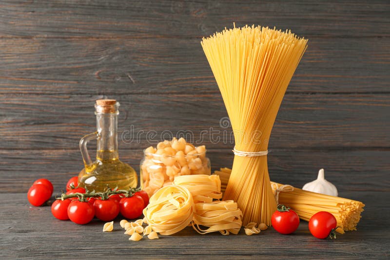 Composition with Pasta, Olive Oil, Tomatoes and Garlic on Wooden Table