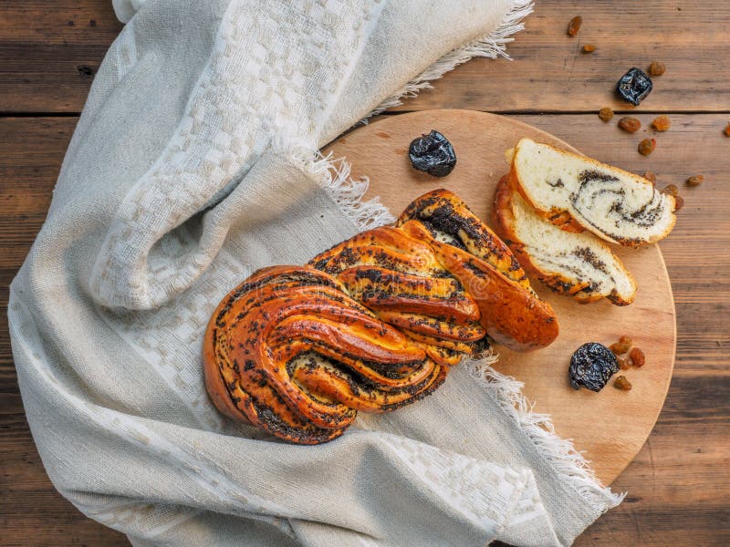 Composition with raisins, prunes on a background of old wood, cloth. Cut sweet twisted bun with poppy seeds. Vintage