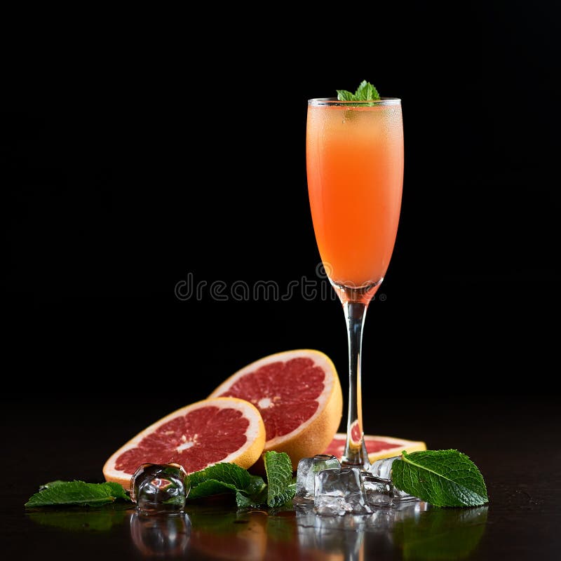 Cocktail glass with cold drink, slices of grapefruit, mint leaves and ice on black background.