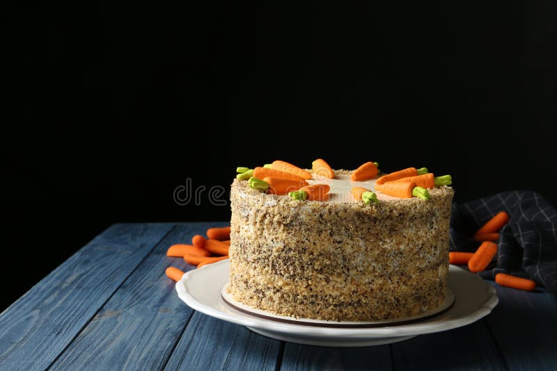 Composizione con il dolce alle carote delizioso sulla tavola di legno blu contro fondo nero immagini stock Composizione con il dolce alle carote delizioso sulla tavola di legno blu contro fondo nero immagini stock
