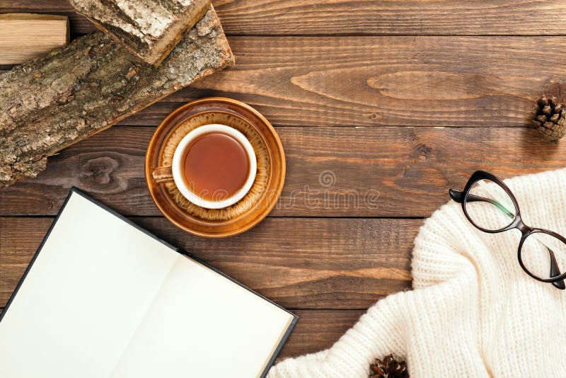 Composizione flaticola in stile Hygge con tazza di tè, libro con pagine vuote, sciarpa bianca a maglia, occhiali da donna, legna