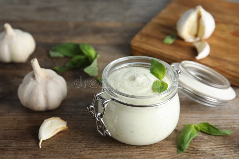 Composition with jar of garlic sauce on wooden table. Composition with jar of garlic sauce on wooden table