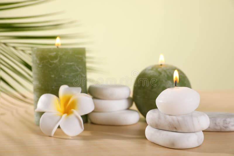 Composição de pedras dos termas e de velas ardentes com a flor na tabela de madeira contra o fundo verde fotografia de stock royalty free Composição de pedras dos termas e de velas ardentes com a flor na tabela de madeira contra o fundo verde fotografia de stock royalty free