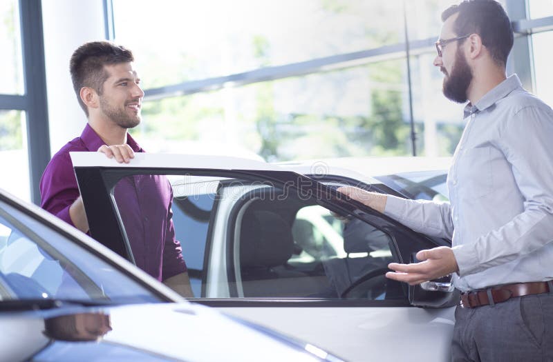 Comprador potencial que fala a um concessionário automóvel ao lado de um carro imagem de stock royalty free Comprador potencial que fala a um concessionário automóvel ao lado de um carro imagem de stock royalty free