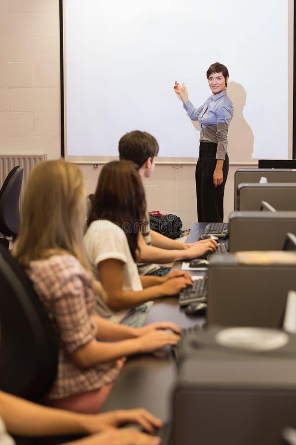 Computer class looking at teacher pointing on projection screen royalty free stock images