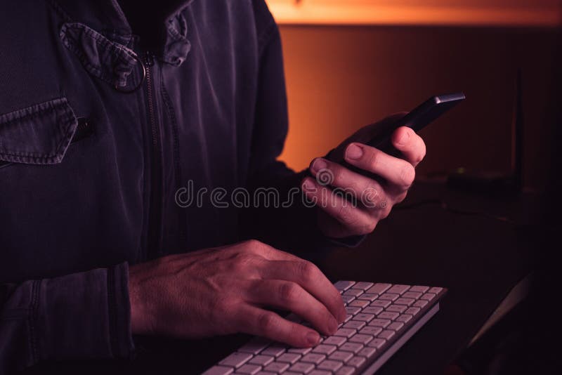 Computer hacker using smartphone device in dark interior, low key with selective focus