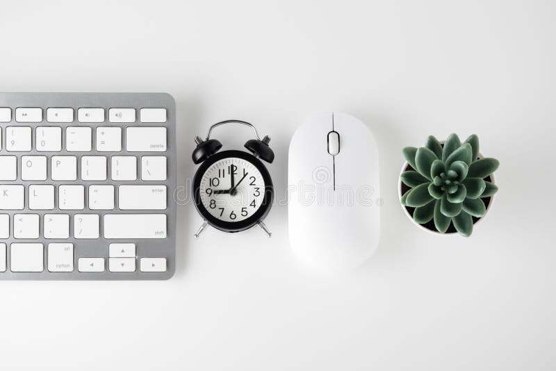 Computer keyboard, mouse and clock on white desk