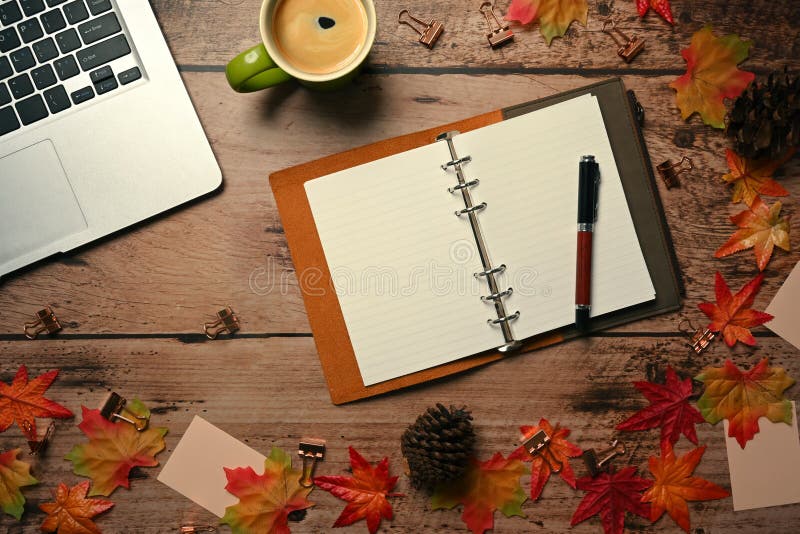 Laptop, empty notebook, coffee cup and autumn maple leaves on wooden table.