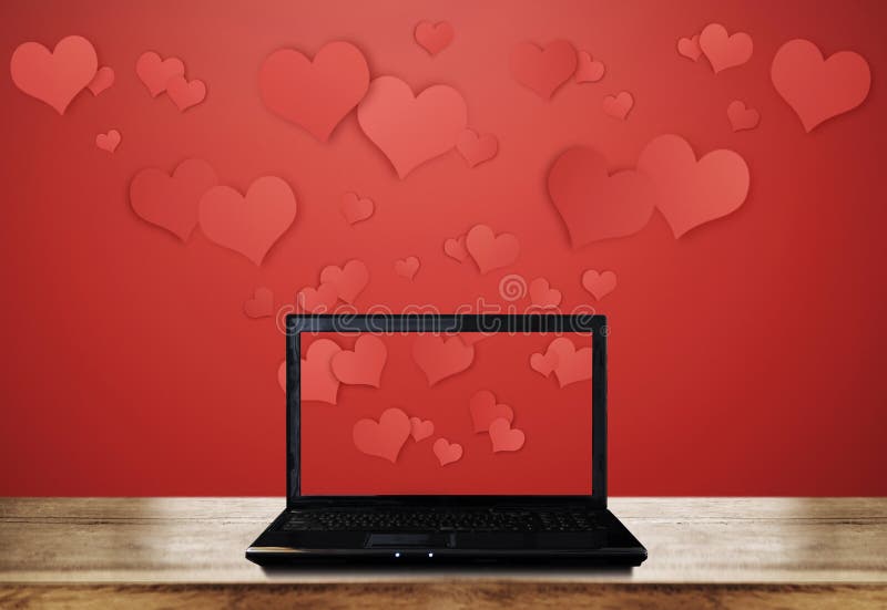 Computer laptop on wooden desk with floating hearts on red background stock photo Computer laptop on wooden desk with floating hearts on red background stock photo