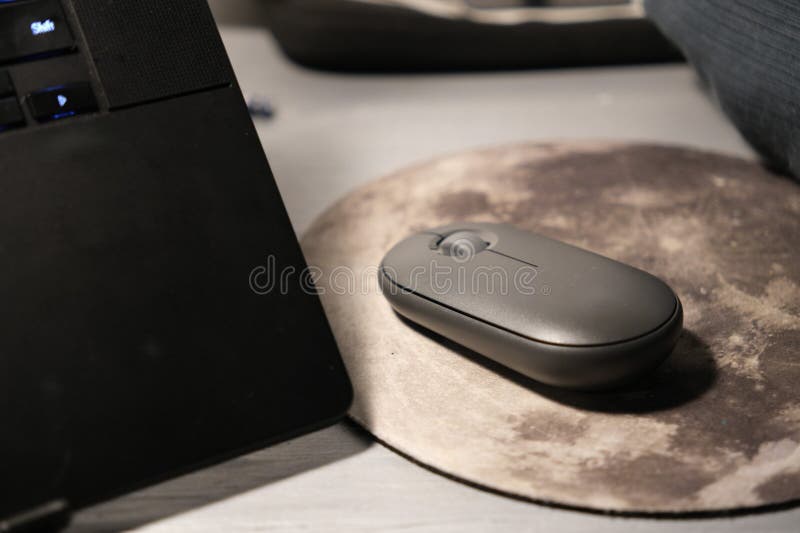 Computer mouse on a moon-shaped mouse pad next to a black laptop. Modern workspace setup illustrating technology, home office, productivity, remote work, digital lifestyle, and desktop accessories. Suitable for editorial and commercial use in tech blogs, articles, e-learning, office content, and lifestyle publications. Laptop personal computer stock images, royalty-free photos and pictures