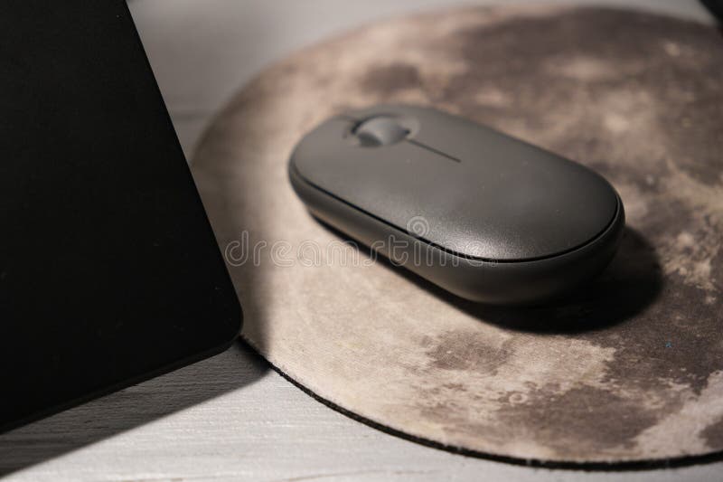 Computer mouse on a moon-shaped mouse pad next to a black laptop. Modern workspace setup illustrating technology, home office, productivity, remote work, digital lifestyle, and desktop accessories. Suitable for editorial and commercial use in tech blogs, articles, e-learning, office content, and lifestyle publications. Laptop personal computer stock images, royalty-free photos and pictures