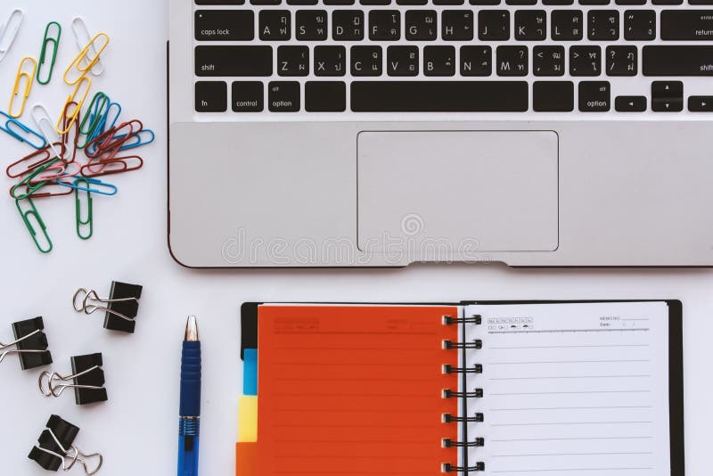 Computer portatile del computer con il taccuino e la graffetta aperti dell'ufficio e penna sullo scrittorio bianco immagini stock