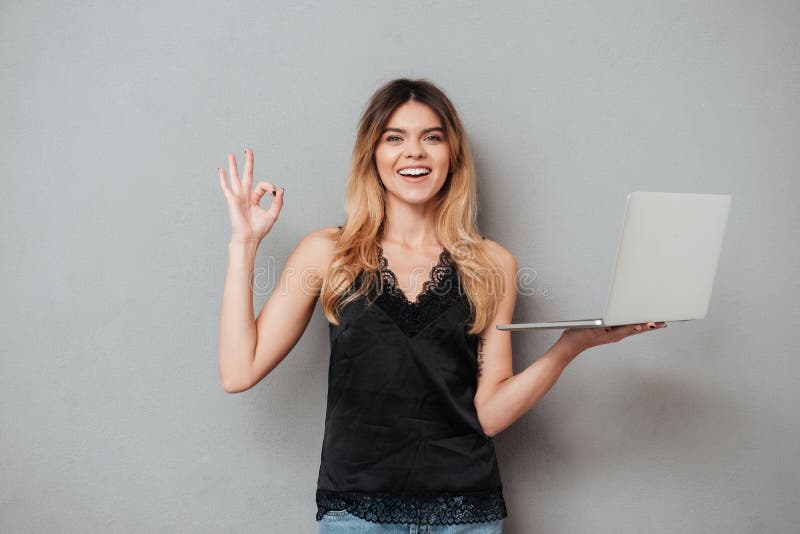Computer portatile sorridente felice della tenuta della donna e gesto giusto di rappresentazione fotografia stock libera da diritti Computer portatile sorridente felice della tenuta della donna e gesto giusto di rappresentazione fotografia stock libera da diritti
