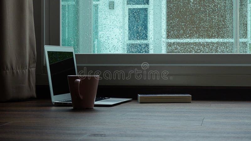 Computernotitieboekje naast een kopkoffie op de regenachtige achtergrond van het dagvenster