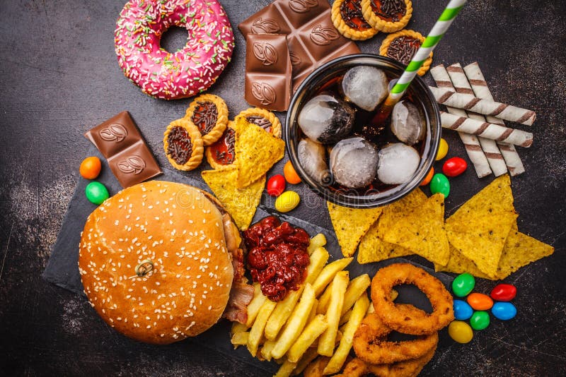 Conceito da comida lixo Fundo insalubre do alimento Fast food e açúcar Hamburguer, doces, microplaquetas, chocolate, anéis de esp