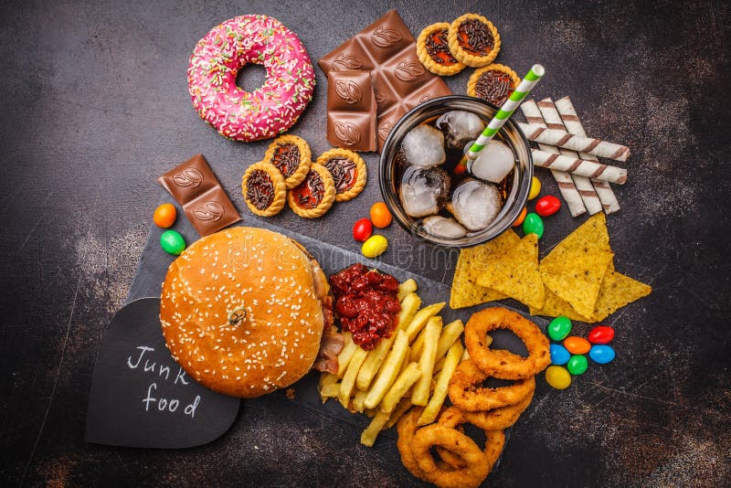 Conceito da comida lixo Fundo insalubre do alimento Fast food e açúcar Hamburguer, doces, microplaquetas, chocolate, anéis de esp