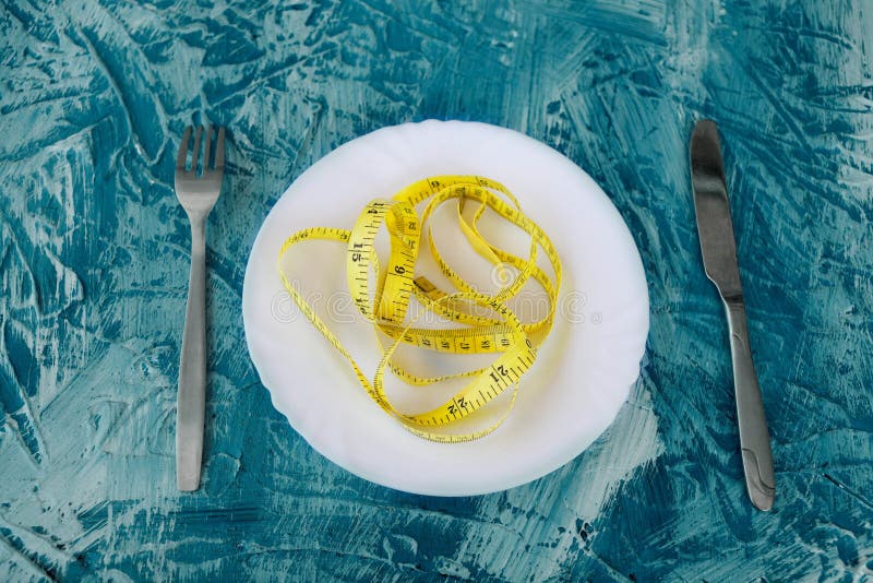 Conceito da dieta - cor amarela de medição da fita na placa vazia no fundo azul imagem de stock Conceito da dieta - cor amarela de medição da fita na placa vazia no fundo azul imagem de stock