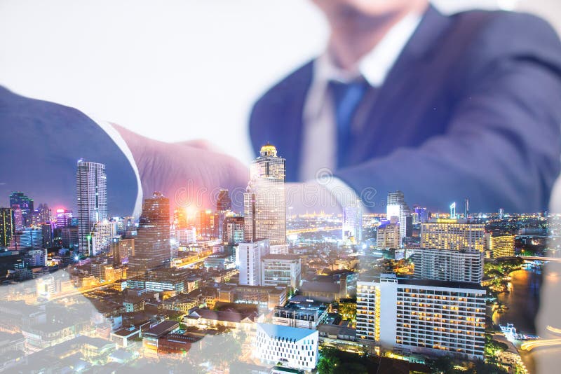 Conceito da exposição dobro Aperto de mão do negócio do acionista com fundo da noite da cidade Homem de negócios que agita as mão imagem de stock royalty free Conceito da exposição dobro Aperto de mão do negócio do acionista com fundo da noite da cidade Homem de negócios que agita as mão imagem de stock royalty free