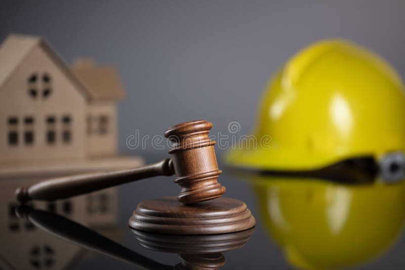 Wooden gavel on the gray background with the house model and the yellow hardhat. Wooden gavel on the gray background with the house model and the yellow hardhat.