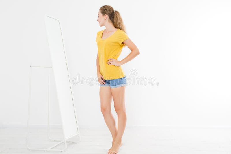 Conceito da venda da compra Menina loura nas calças de brim e na camisa de t A jovem mulher na boa forma do corpo que olha o espe imagem de stock Conceito da venda da compra Menina loura nas calças de brim e na camisa de t A jovem mulher na boa forma do corpo que olha o espe imagem de stock