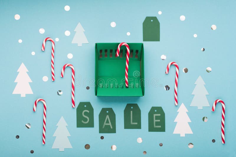 Sale text with green gift box and Christmas candy canes on blue paper background. Design for promotion of winter end of year sale. Top view, copy space. Super sale 12/12 concept. Sale text with green gift box and Christmas candy canes on blue paper background. Design for promotion of winter end of year sale. Top view, copy space. Super sale 12/12 concept