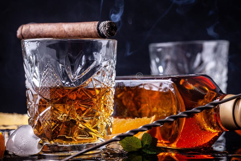 Conceito do alcoolismo, solidão, dependência Uma garrafa do uísque, de um vidro do uísque e com gelo, um charuto com fumo em um p imagem de stock Conceito do alcoolismo, solidão, dependência Uma garrafa do uísque, de um vidro do uísque e com gelo, um charuto com fumo em um p imagem de stock