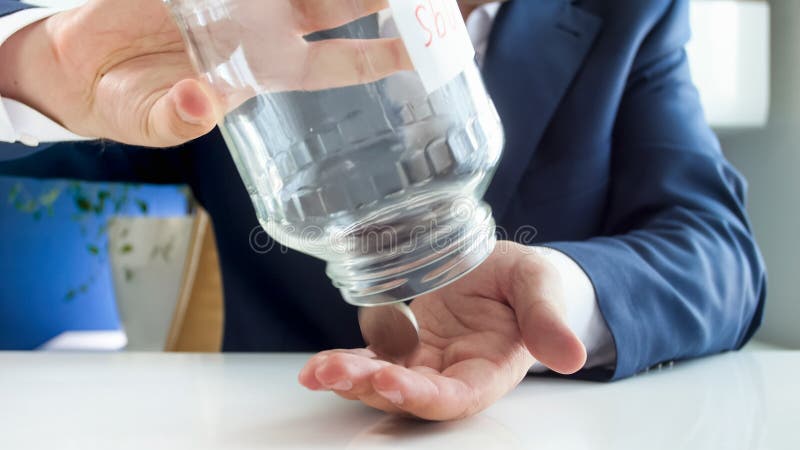 Conceito do crisi financeiro Foto do close up do frasco de vidro emtying do homem de negócios novo com moedas foto de stock Conceito do crisi financeiro Foto do close up do frasco de vidro emtying do homem de negócios novo com moedas foto de stock