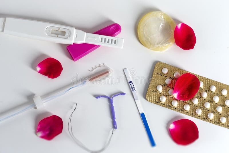 Conceito do DIU do símbolo do controlo da natalidade e comprimidos contraceptivos e preservativo com pétalas cor-de-rosa