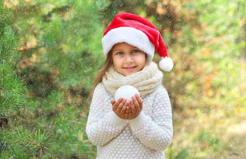 Conceito do Natal e dos povos - criança de sorriso pequena da menina no chapéu de Santa com bola de neve fotografia de stock royalty free Conceito do Natal e dos povos - criança de sorriso pequena da menina no chapéu de Santa com bola de neve fotografia de stock royalty free