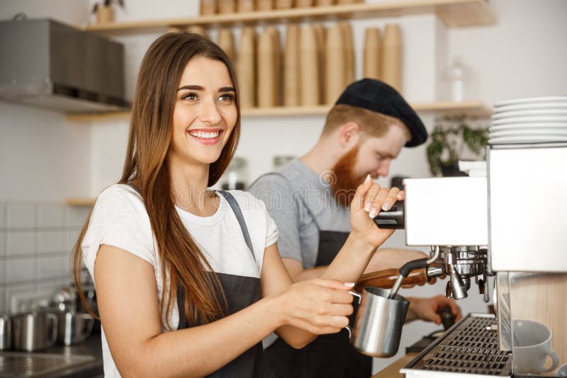 Conceito do negócio do café - retrato do barista da senhora no avental que prepara e que cozinha o leite para a ordem do café com foto de stock Conceito do negócio do café - retrato do barista da senhora no avental que prepara e que cozinha o leite para a ordem do café com foto de stock
