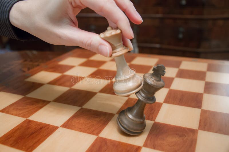 Conceito: a mulher que domina o homem A m?o de uma mulher d? o checkmate ao rei com a rainha em um tabuleiro de xadrez de madeira foto de stock royalty free Conceito: a mulher que domina o homem A m?o de uma mulher d? o checkmate ao rei com a rainha em um tabuleiro de xadrez de madeira foto de stock royalty free