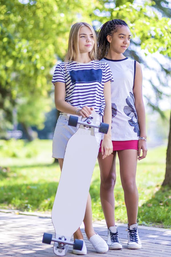 Conceitos do adolescente Duas amigas adolescentes junto com Longboard fora no parque imagem de stock Conceitos do adolescente Duas amigas adolescentes junto com Longboard fora no parque imagem de stock