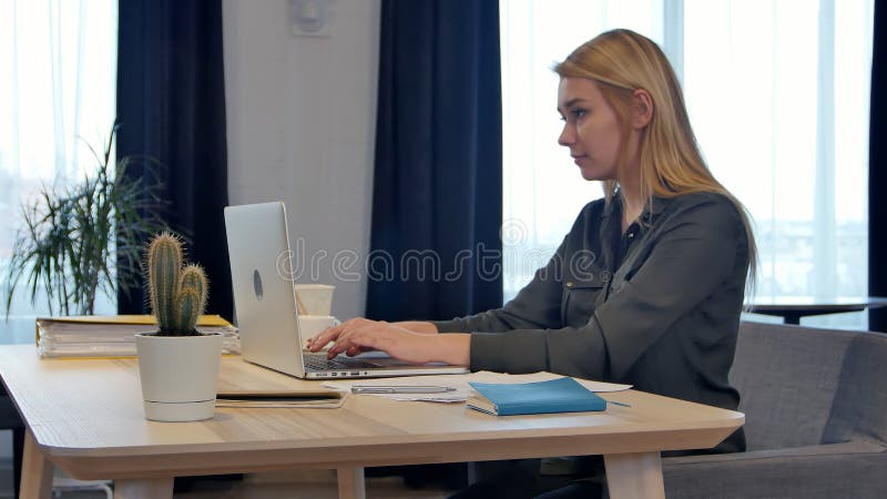 Concentrado en el trabajo, mujer joven confiada en la ropa de sport elegante que trabaja en el ordenador portátil mientras que se imagenes de archivo Concentrado en el trabajo, mujer joven confiada en la ropa de sport elegante que trabaja en el ordenador portátil mientras que se imagenes de archivo