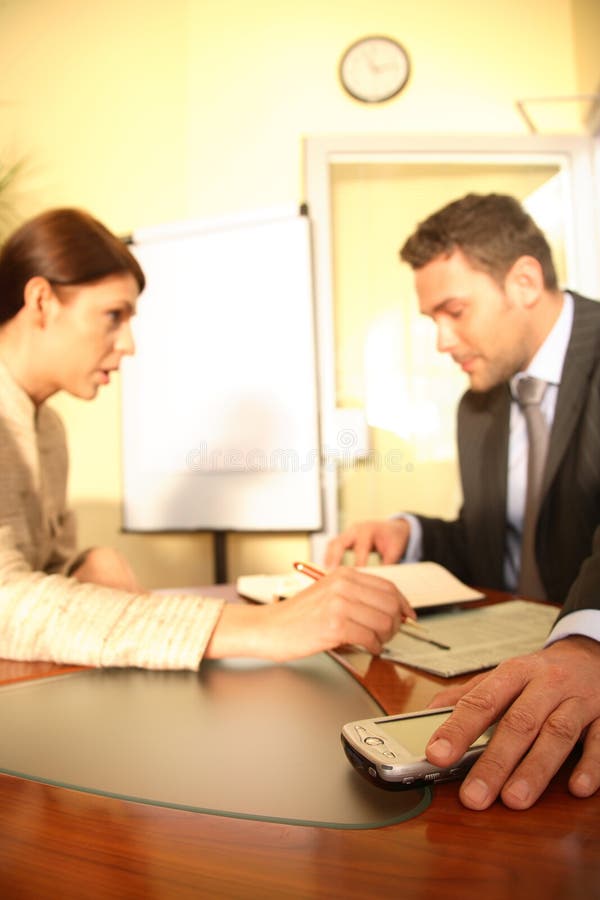 Imprenditore seduto a un tavolo mette un dispositivo elettronico da parte per concentrarsi sul lavoro oggetto di discussione con una collega.