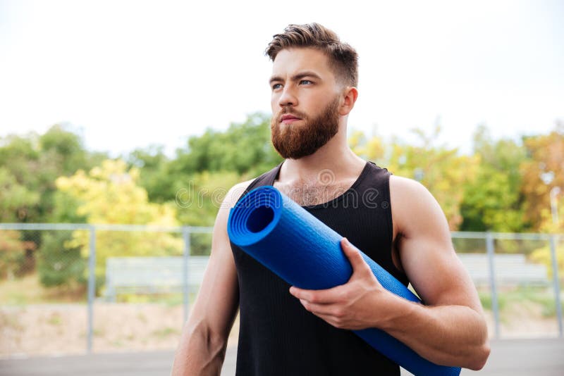 Concentrated Serious Male Yoga Instructor Holding Mat Stock Image