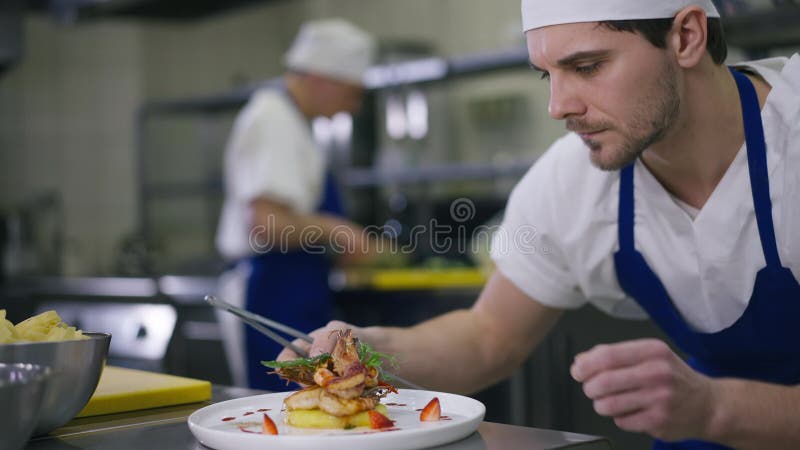 Concentrated young cook decorating seafood with greenery in slow motion turning plate with dish. Portrait of