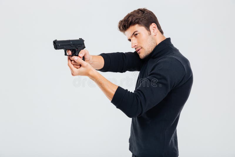 Concentrated young man standing and aiming with gun