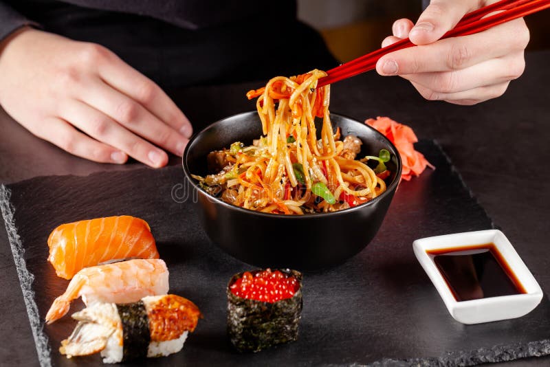 Concept of Asian cuisine. The girl is holding Japanese chopsticks in her hand and eating Chinese noodles from a black plate